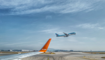 Tip of passenger plane wing in airport with plane taking off in the background